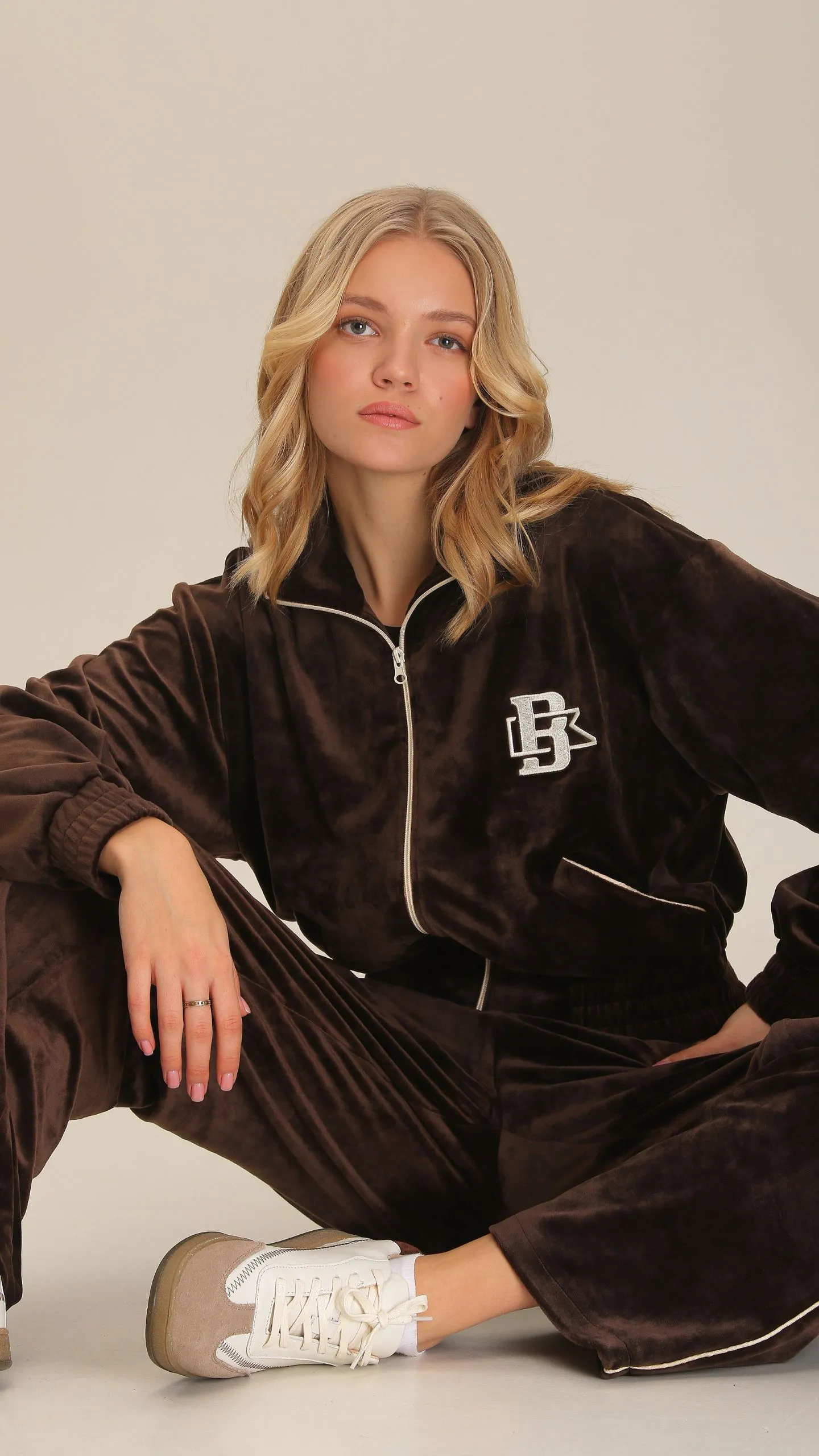 Дівчина у темно-шоколадному вельветовому костюмі та білих кросівках сидить