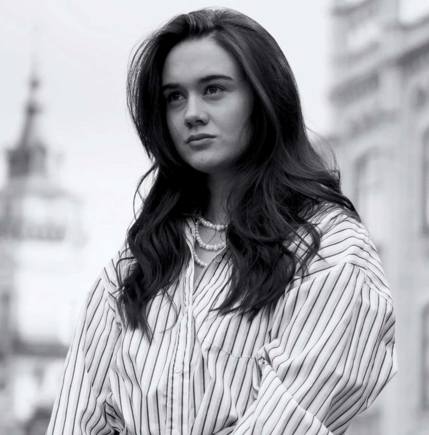 Монохромний портрет дівчини в смугастій сорочці та перловому намисті, яка дивиться вбік
