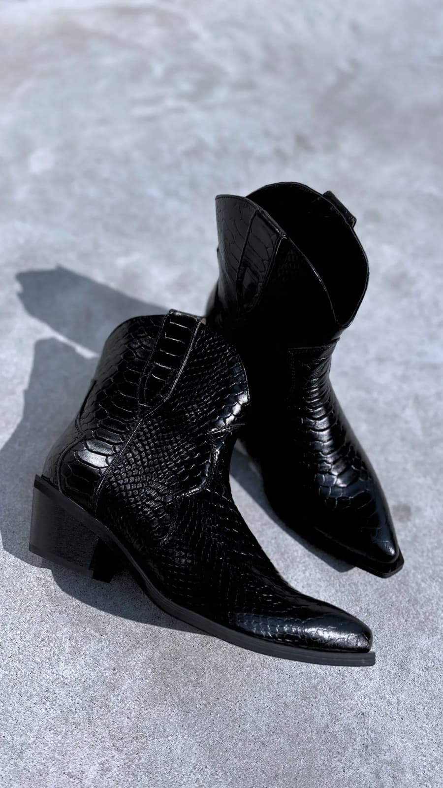 Пара чорних шкіряних казаків із тисненням під рептилію на бетоні — вигляд зверху під кутом. (зображення 1 з 3)